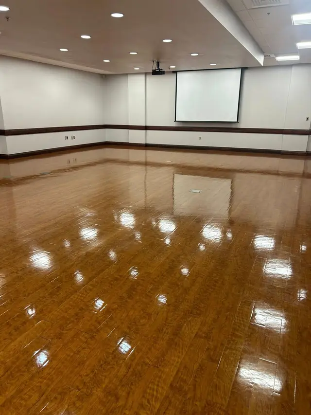 An emptied auditorium with a freshly buffed hardwood look floor and the projector screen down