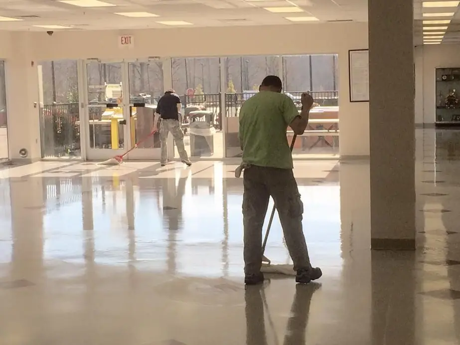 Two crew members mopping a large lobby floor beside glass entrance doors