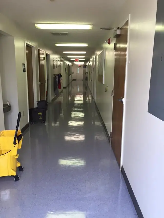 A clean corridor with a yellow mop bucket and a cleaning cart parked to one side