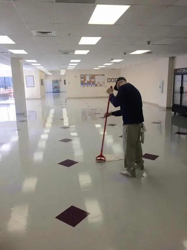 A crew member dust mopping a large open plan office floor near the vending machines