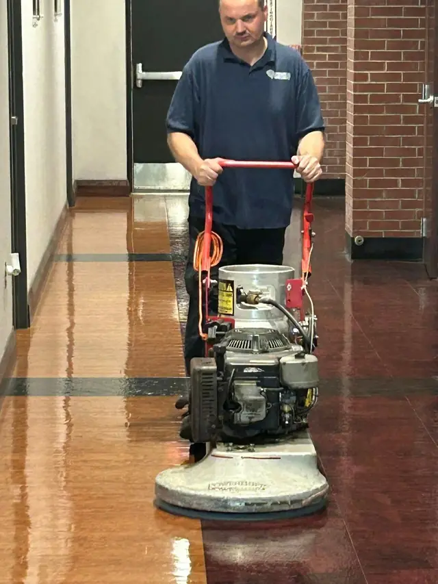 A Commercial Maintenance Specialist technician running a floor buffer along a brick walled corridor