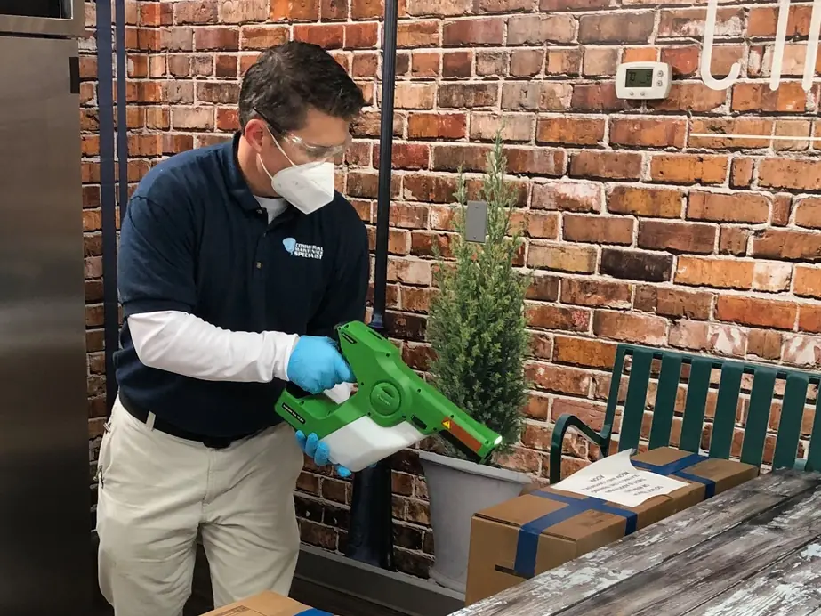A technician in mask, goggles and gloves using an electrostatic disinfecting sprayer